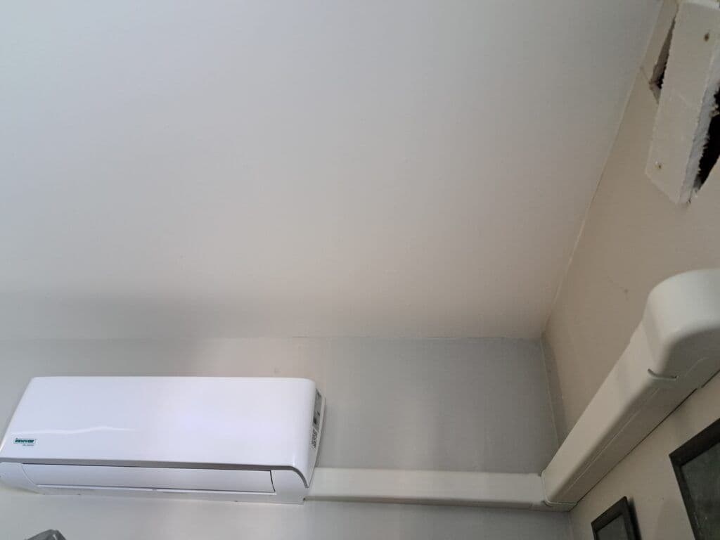 Air conditioning unit installed on wall with visible piping and ceiling corner.