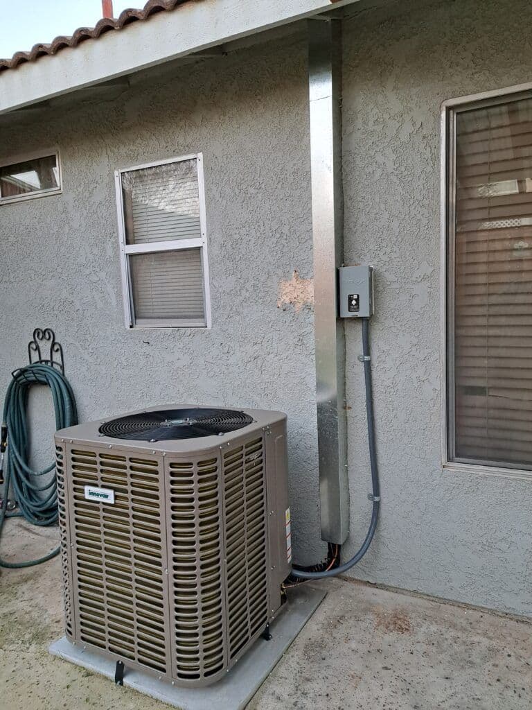 Residential central air conditioning unit installed outside a gray textured wall.