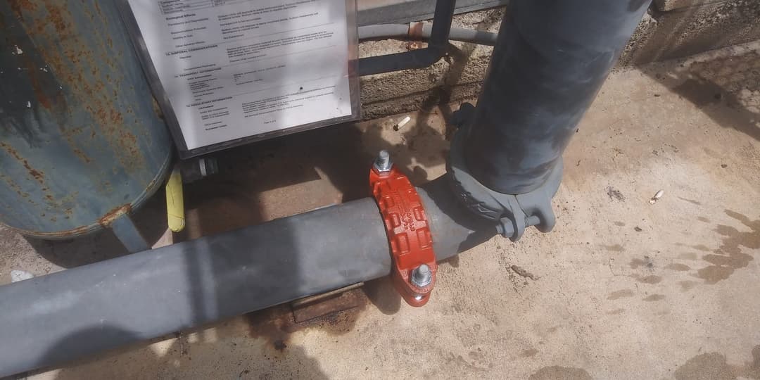 Red valve clamp on a gray pipe next to an industrial container and maintenance documentation.