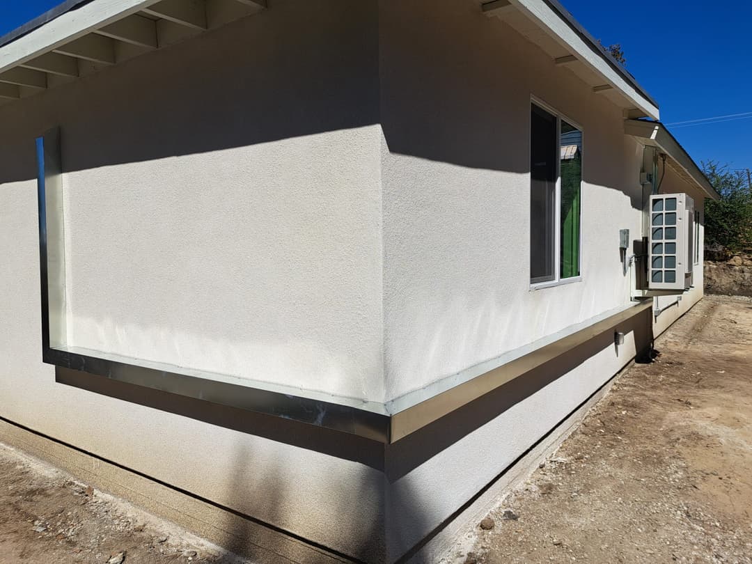 Residential home exterior with textured white walls, modern windows, and paved foundation.