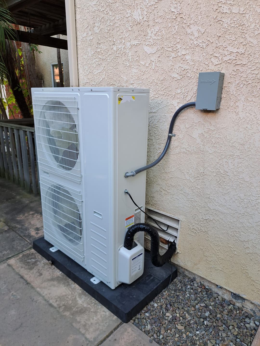 Outdoor air conditioning unit installed against a textured wall with power connections.