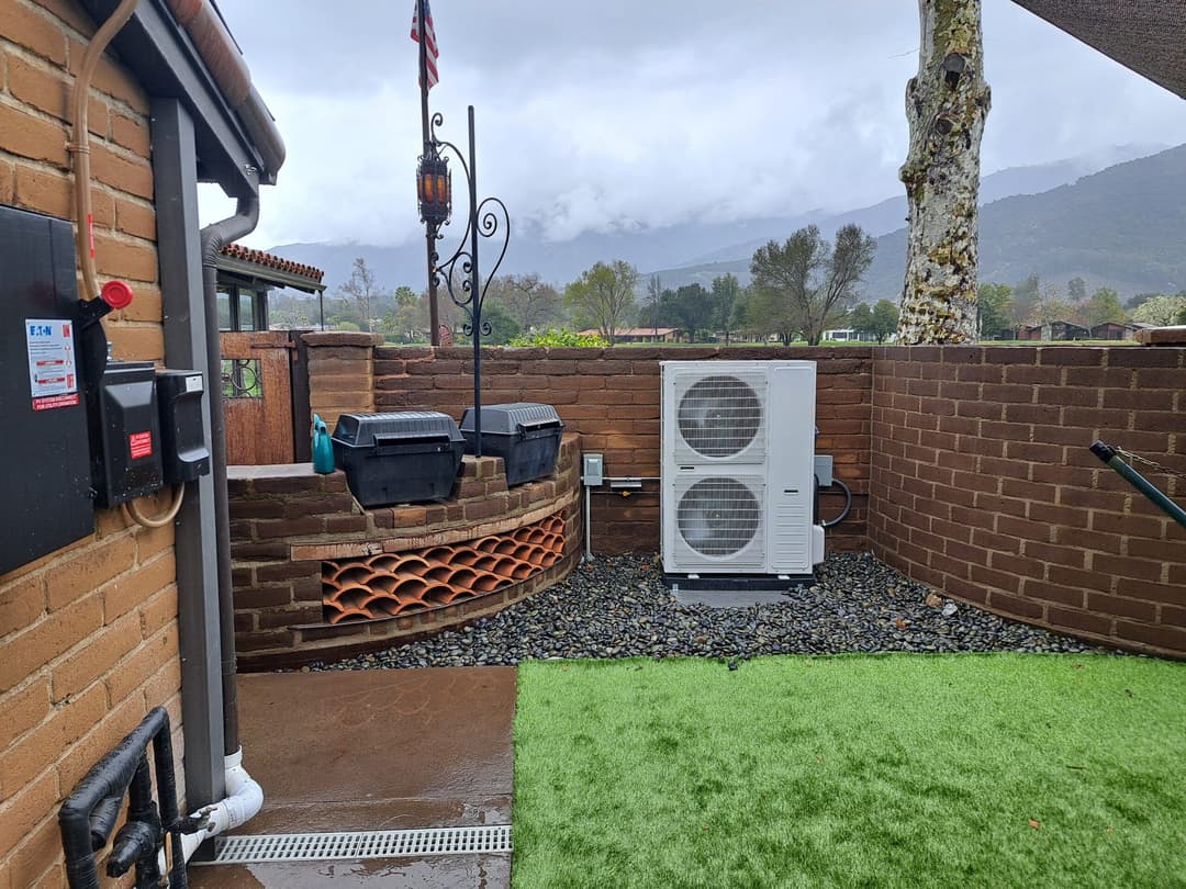 Outdoor air conditioning unit installed on gravel beside a brick wall in a landscaped area.
