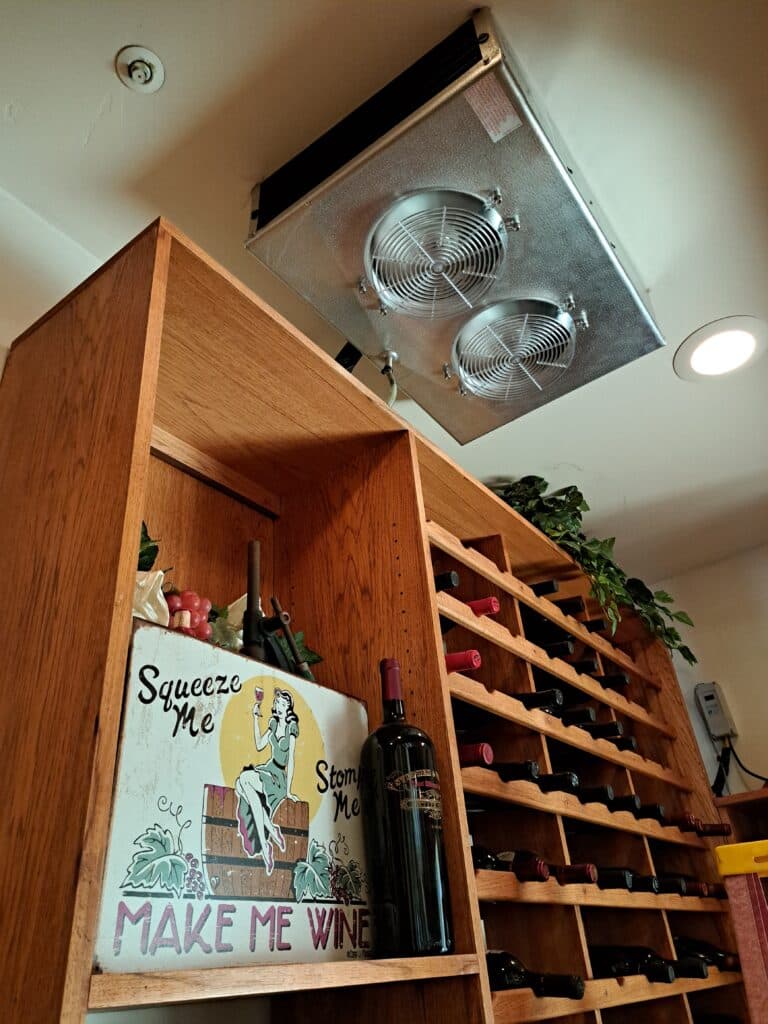 Wine storage area featuring a wall-mounted cooling unit and decorative sign.