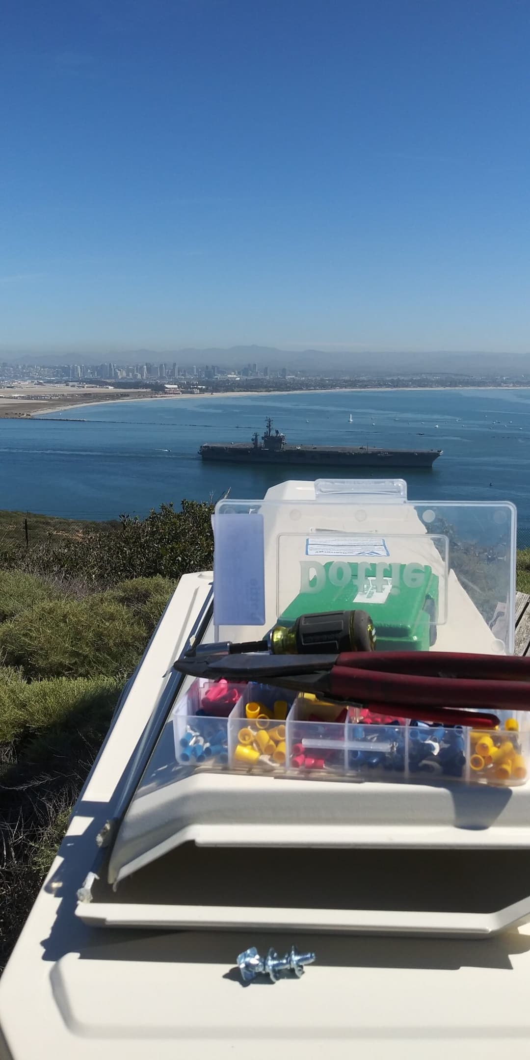 Tools and supplies on a hilltop overlooking a ship and city skyline by the water.