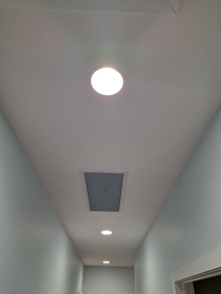Modern ceiling lights and air vent in a hallway with light blue walls.