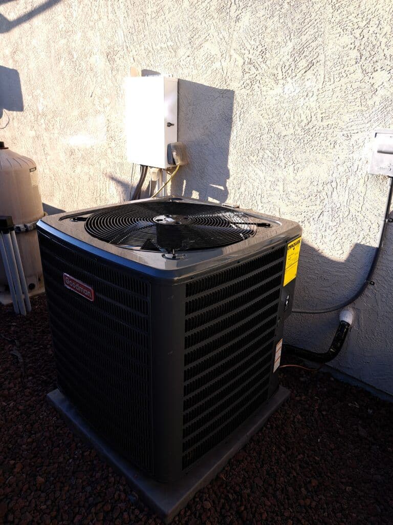 Outdoor air conditioning unit installed on a concrete pad against a textured wall.