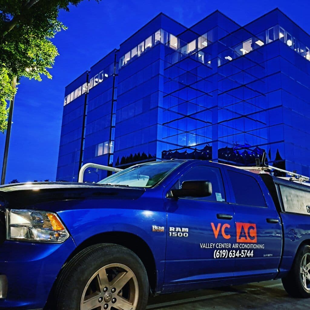 Blue RAM 1500 truck for Valley Center Air Conditioning near modern glass office building at night.