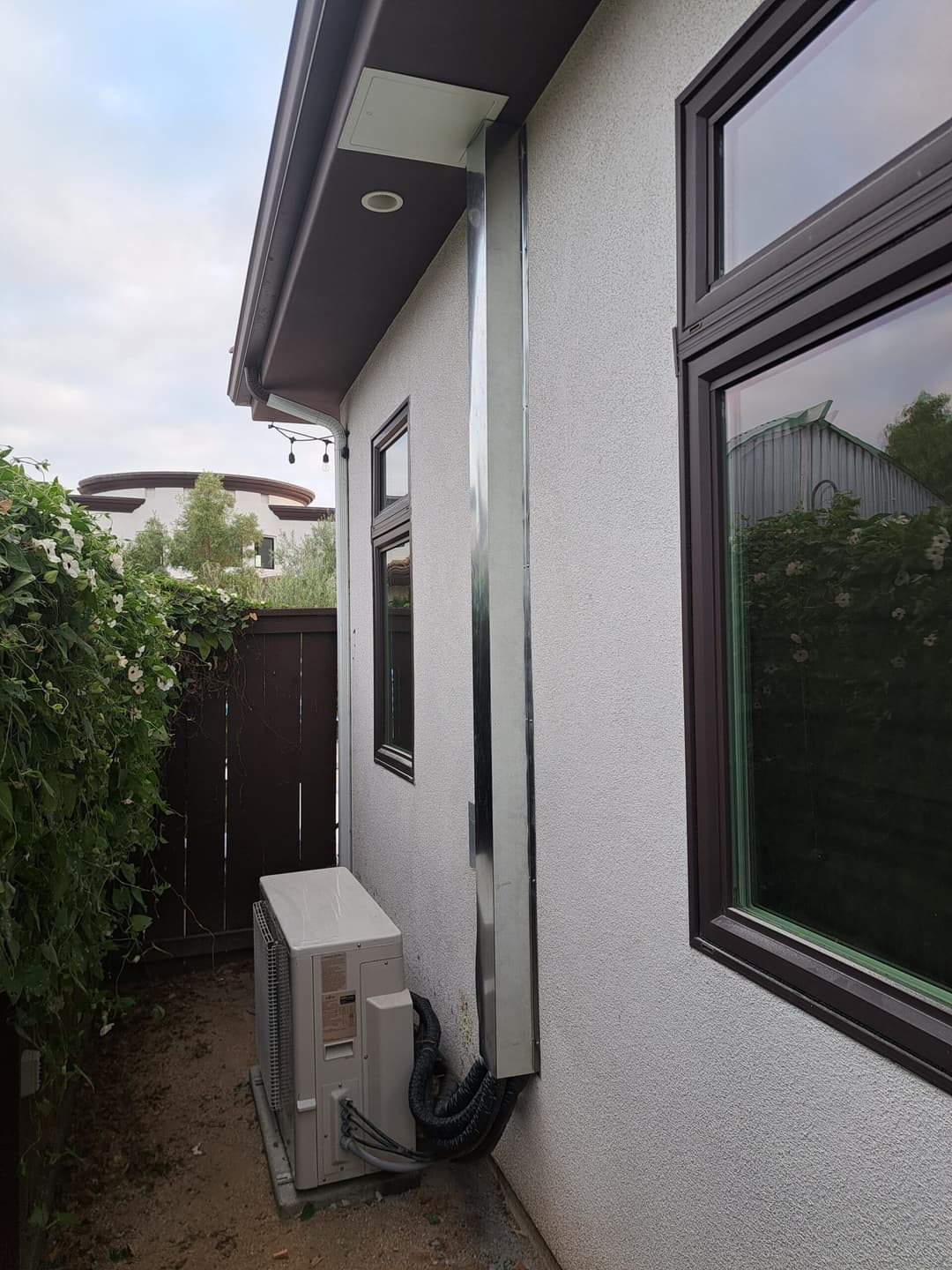 Exterior view of a home featuring a sleek metal conduit and air conditioning unit.