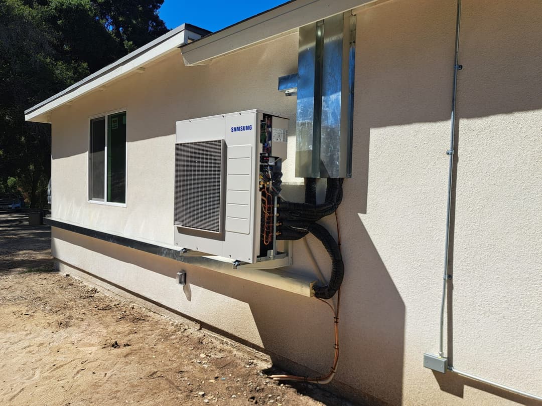 Samsung air conditioning unit installed on the exterior wall of a home, showcasing plumbing and connections.