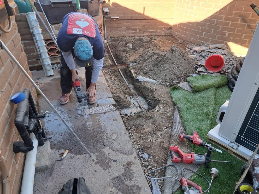 Person using a drill in a construction area with tools, dirt, and equipment around.